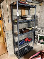 Full view of gray modular plastic shelving unit against basement concrete wall with various items on shelves (contents not included in sale).