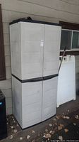 Front view of tall beige plastic outdoor storage cabinet with scuffs and dirt marks.