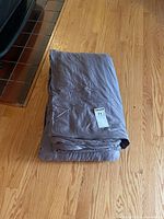 Folded gray weighted blanket lying on hardwood flooring with a MaxSold lot sticker on top.