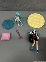 Two anime figures with multiple bases and cushions displayed on a gray surface