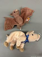 Top view of Batty the Bat (brown wings, tail) and Knuckles the Ram (cream colored with blue ribbon) Ty Beanie Baby plush toys on a gray surface.