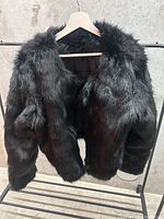 Front and side view of black fur jacket hanging on a rack showing dense, shiny fur covering the exterior.