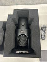 Blue Yeti X microphone in black color resting in protective foam packaging next to USB cable.