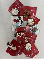 Photo showing ten Christmas badges including Santa heads, snowmen, wreath, and crystal decorations on red backing cards arranged on a white surface.