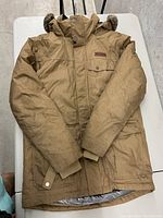 Full front view of the brown Columbia men's winter jacket showing hood with faux fur trim, multiple front pockets, and button details