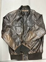 Front view of brown leather jacket laid flat, showing snap-button chest pockets and rib-knit cuffs and waistband.
