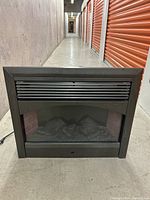 Front view of black electric fireplace insert showing vented grille and interior faux logs.
