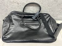 Front view of black croc embossed faux leather duffel bag with dual handles, fabric shoulder strap, and tag still attached