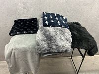 Five large fleece and plush throws folded and arranged on a metal rack against a gray backdrop.
