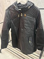 Front view of black Michael Kors jacket showing quilted design, front zipper, hood, and pockets.
