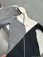 Tri-color Oakley ski jacket laid flat with hood up, showing jacket front and zipper.
