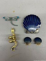 Set of costume jewelry including a large blue scallop shell brooch, two smaller matching shells, a dragonfly brooch with turquoise detailing, and a gold-tone snake ring.