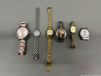 All six watches lined up flat on a gray surface showing variety in size, metal color, and style