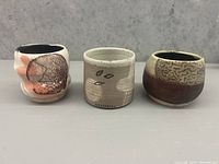 Front view of the three hand made pottery pots with varying designs and colors against grey background.