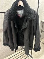Front view of Vince Camuto black jacket with faux shearling collar and lining hanging on rack.