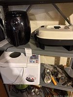 Photo showing the Elite Gourmet air fryer, beige and black electric frying pan, white Select Edition bread maker, and metal manual meat grinder with attachments.