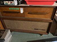 Full view of vintage wooden cabinet with woven speaker grille and wooden handles.