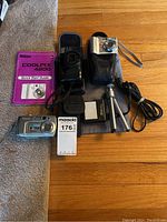 All cameras, guides, and accessories laid out on wooden floor and carpet edge visible