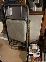 Photo showing stacked folding chairs with padded beige seats and nearby boxed games including an abacus kit and chess/checkers set