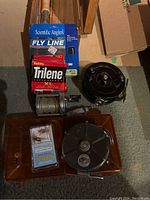 Fishing reels, fishing line packages, and fishing hooks arranged on floor.