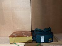 Fishing tackle box and outdoor gear bag side by side on floor against a wall.