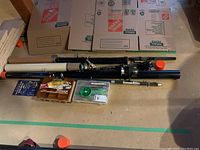 Fishing rods, rod tubes, lures, fishing line, and tackle boxes laid on a concrete floor with cardboard boxes behind.