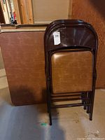 Photo showing the folded card table with brown vinyl top and four stacked folding chairs with brown vinyl seats and backs, all with brown metal frames.