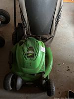Top view of green Lawn Boy gas powered push mower with attached cloth grass catcher bag. Unit shows signs of use and dirt, cloth bag has visible wear.