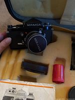 Miranda G camera body with lens and front lens cap inside padded carrying case with instruction manual and red film canister.