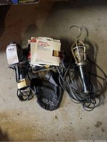 Photo showing Craftsman orbital sander, handheld work light, power cords tangled, sanding disc packages on concrete floor