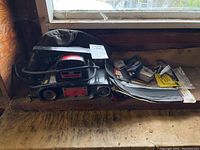 Side view of the belt sander with attached dust collection bag and various small accessories and papers around it.