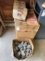 Stacked original boxes including Air King SU05 control, Furnas heater insert box, Hanko Finland packaging, instruction booklet, with sauna stones in front.