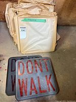 Photo showing stacked plexiglass sheets wrapped in paper with vintage Walk/Don't Walk signs in front.