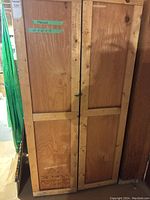 Front view of the plywood storage cabinet with two doors closed, showing latch and wood texture.