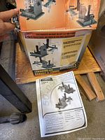 View of the original cardboard box showing printed product images of the tenoning jig and the instruction sheet placed on the floor.