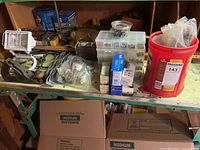 Photo showing various tools and hardware items on a workbench with nails in containers, a red bucket, and other miscellaneous items.