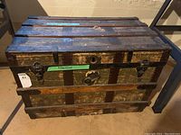Front view of vintage wooden trunk showing metal reinforcements, two clasps, central lock, and wood surface wear.