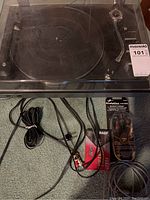 View of JVC turntable on carpeted floor showing platter, tonearm, control knobs, and dust cover in open position. Power adapter and cables laid out in front.