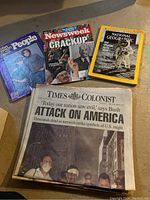 Vintage magazines and newspapers spread on floor, showing covers of People, Newsweek, National Geographic, and Times Colonist from 9/11