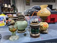 Five antique lamps displayed on a table including oil and hurricane lamps, with some showing dust and wear.