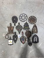 Full layout of 13 metal trivets on a concrete floor showing size and variety.