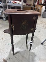 Full view of the antique wooden smokers stand, showing the overall shape, legs, side shelf, and floral decoration on the door.