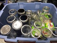 Bin of various Ball Mason canning jars including clear and amber glass jars with metal lids.