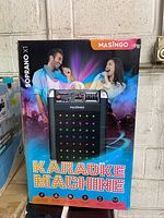 Front view of the box showing the Soprano XI karaoke machine image and branding with a graphic of a man and woman singing.