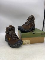 Side angle view of brown Keen hiking boots on and beside their original green and brown box showing tread and general build.