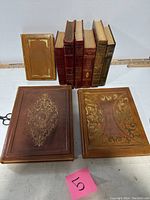 Nine leather bound books displayed showing covers and spines, highlighting gold gilt decorations and condition.