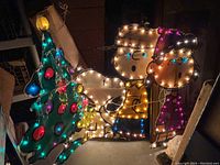 Group of 3 lighted outdoor Peanuts characters and Christmas tree, illuminated at night showing colorful bulbs and character details.