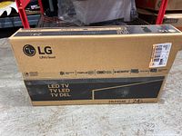 Front view of sealed original cardboard packaging of LG 24" LED TV with model number and key features visible.
