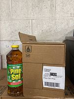 View of one Pine-Sol bottle with yellow cap and label showing product details in front of opened cardboard box.