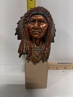 Front view of the Sitting Bull bust showing facial details, headdress paint, and top of heavy stone base.